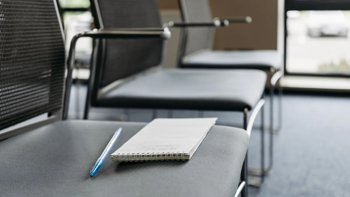 Open notebook and pen resting on an empty chair in a bare meeting room