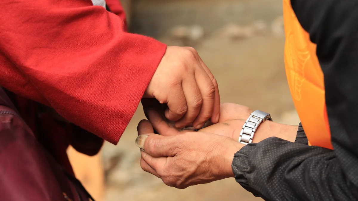 Close-up of two people exchanging small items with hands against a blurred outdoor background.
