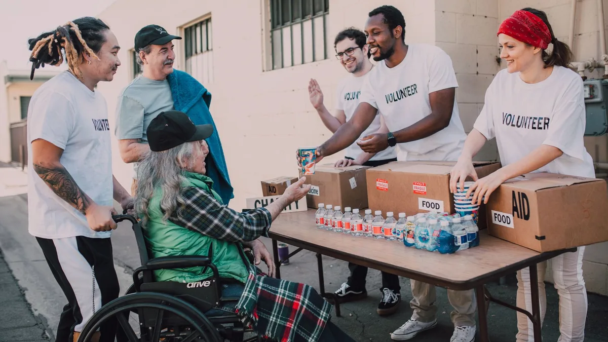 Volunteers distribute bottled water and supplies to diverse individuals in an outdoor setting.